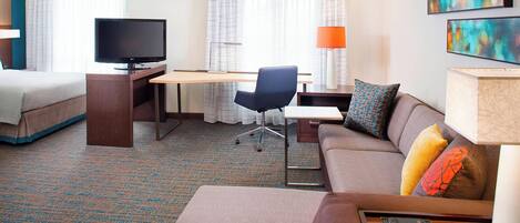 Una habitación de hotel con cama, escritorio con televisor, sofá y lámpara.