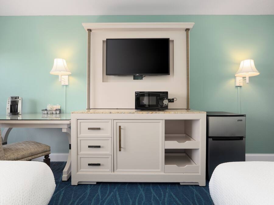 Habitación de hotel con dos camas, un escritorio, un televisor de pantalla plana, un microondas y un refrigerador.