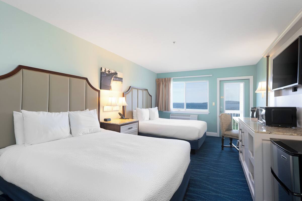 A hotel room with two beds, a desk, a chair, a television, and a window with a view.