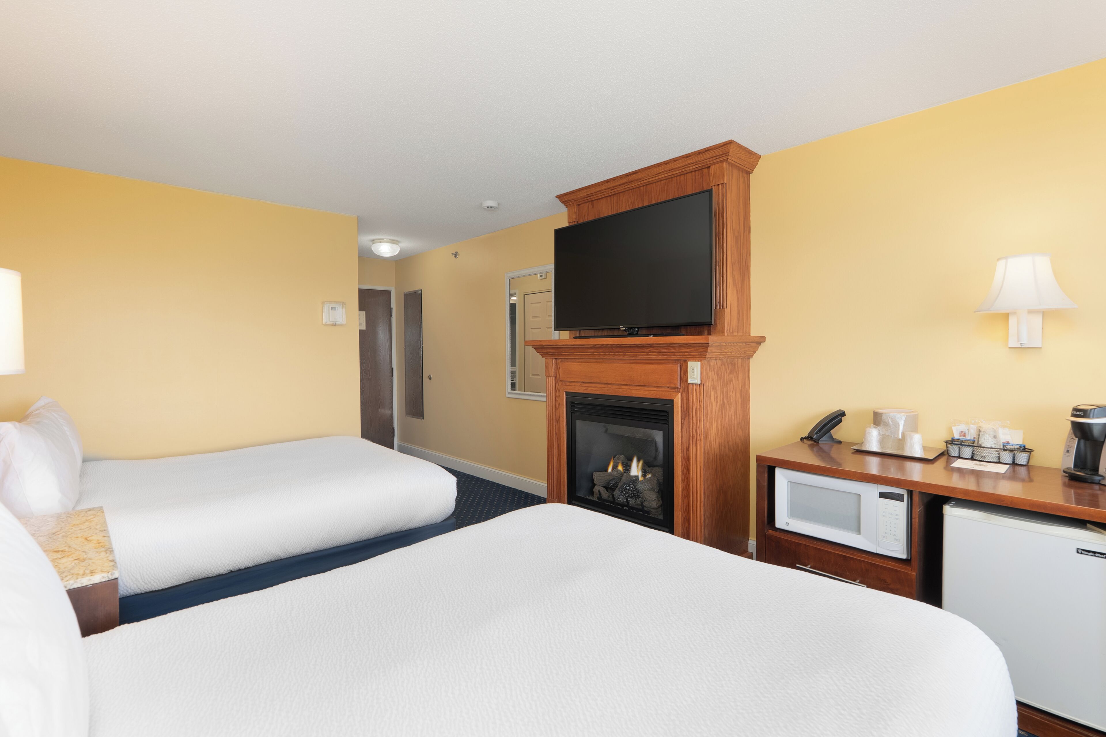A hotel room with two beds, a fireplace, a television, a microwave, and a coffee maker.