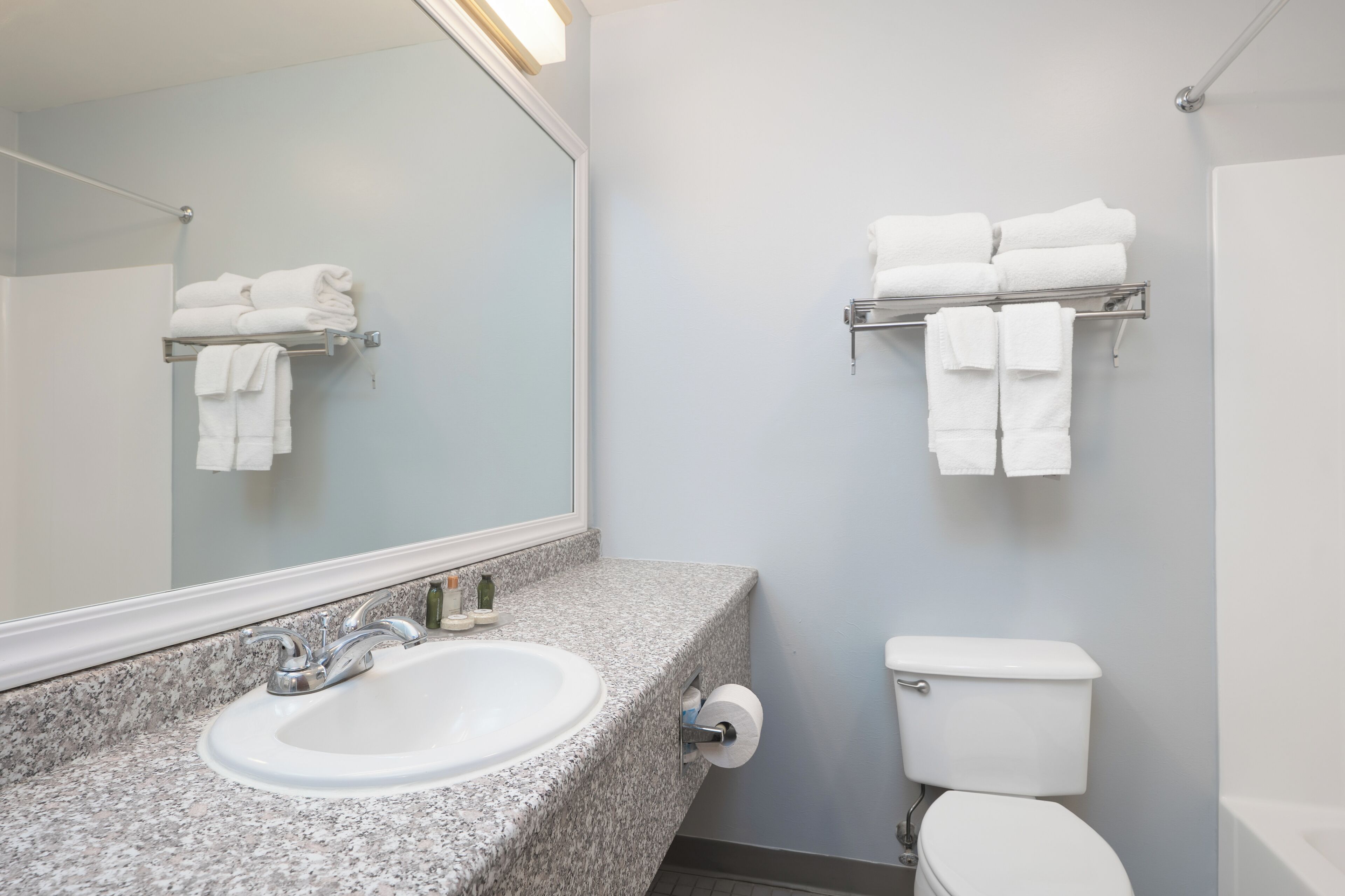 Un baño con lavamanos de encimera de granito, inodoro y toalleros en la pared.