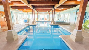 A swimming pool with a wooden ceiling and tiled floor, surrounded by lounge chairs and a sun chair. - Fireside Inn & Suites - Belfast (Belfast)