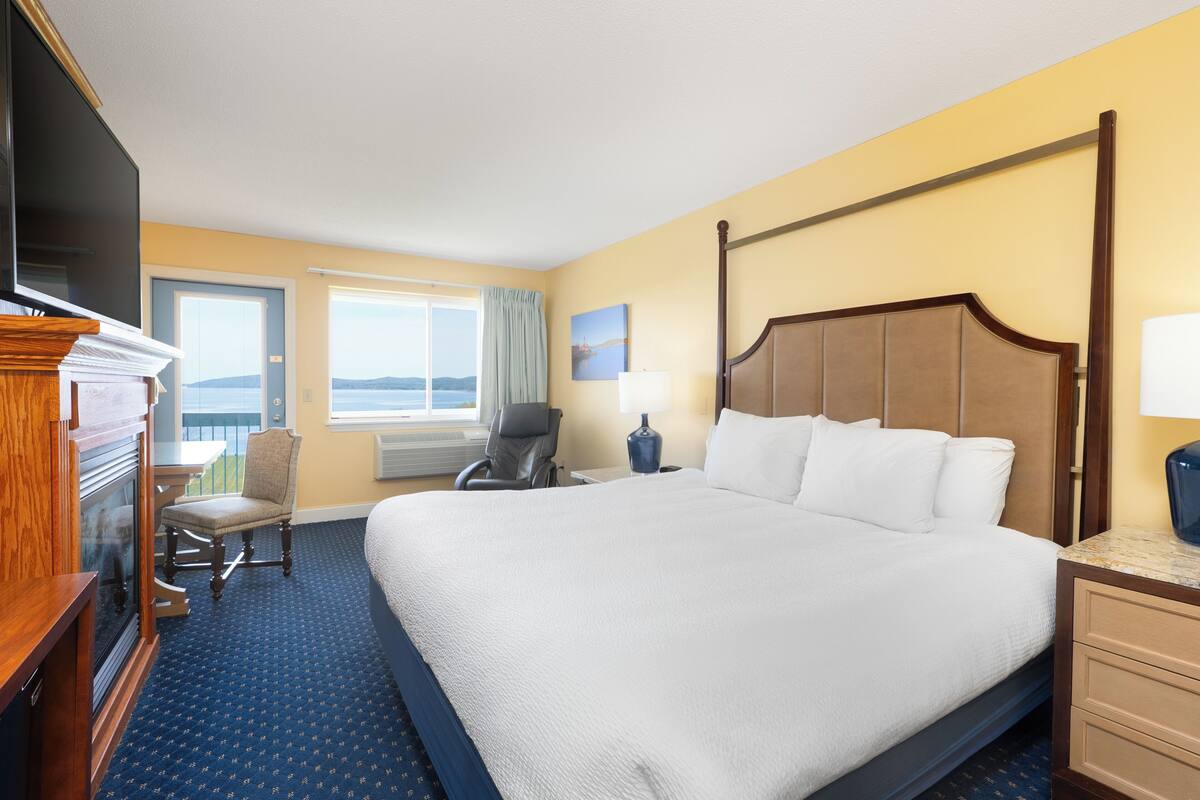 A hotel room with a large bed, a television, a chair, a desk, and a window with a view of the sea.