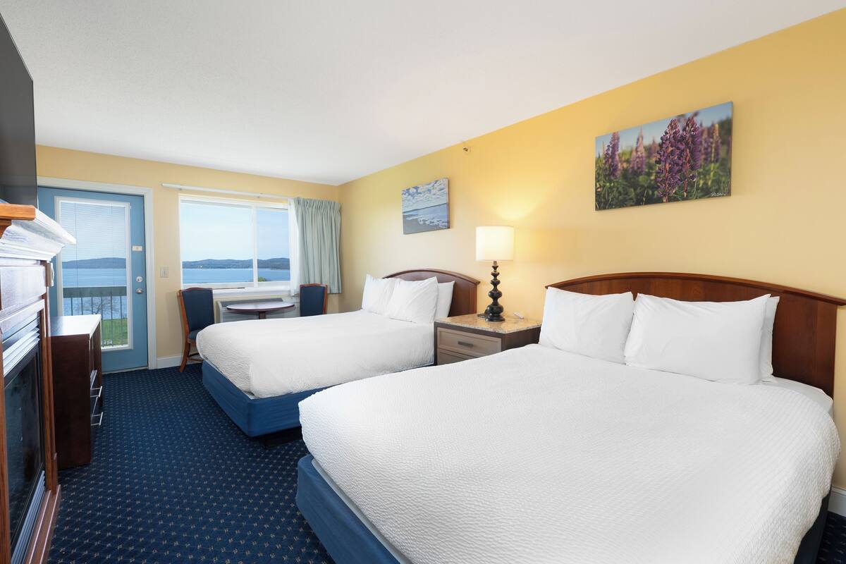 A hotel room with two beds, a desk, a chair, and a view of the sea.