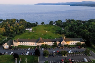Vista aérea de um hotel com estacionamento, um gramado e um corpo d'água ao fundo.