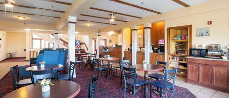 A hotel lobby with multiple seating areas, a staircase, and a kitchen area.