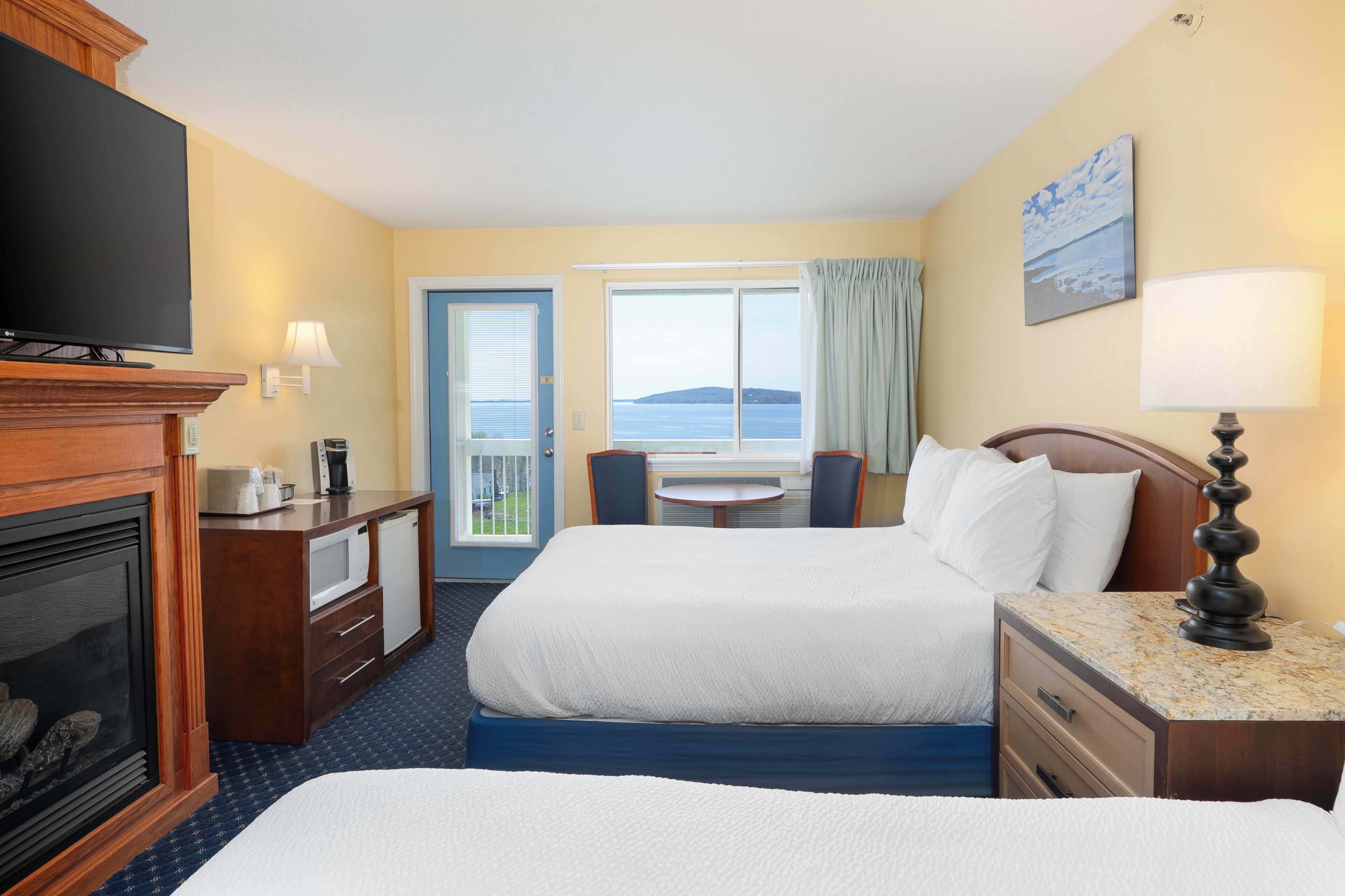 Une chambre d’hôtel avec deux lits, une télévision, une cheminée, un bureau avec une lampe et une vue sur la mer.