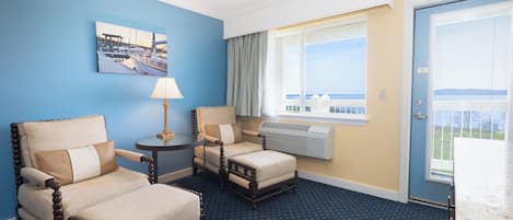 A hotel room with two armchairs, a small table, a lamp, a window with a view, and an air conditioning unit.