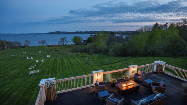 A patio with outdoor furniture and a fire pit overlooking a grassy area and water body. - Fireside Inn & Suites - Belfast (Belfast)