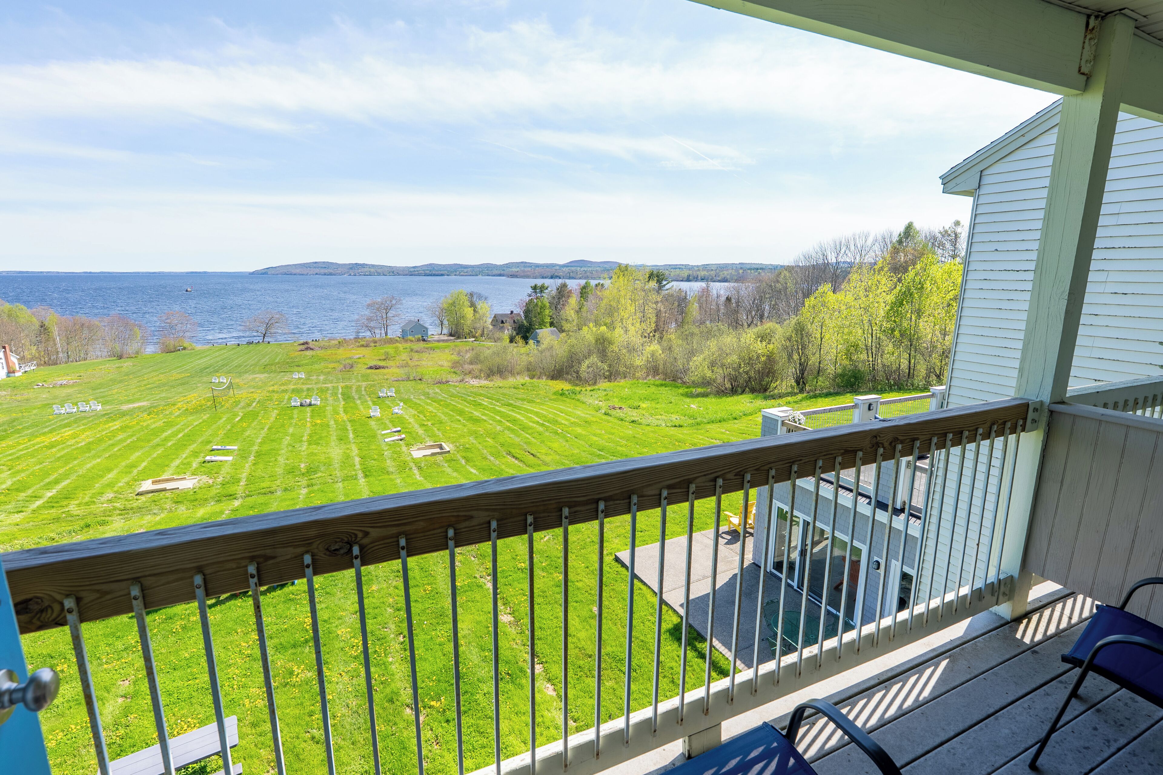 A balcony with a view of a grassy field, a body of water, and distant hills.