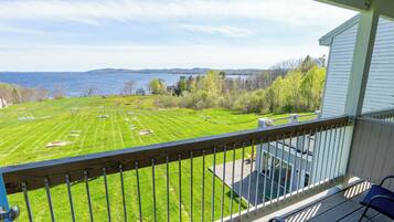 A balcony with a view of a grassy field, a body of water, and distant hills.
