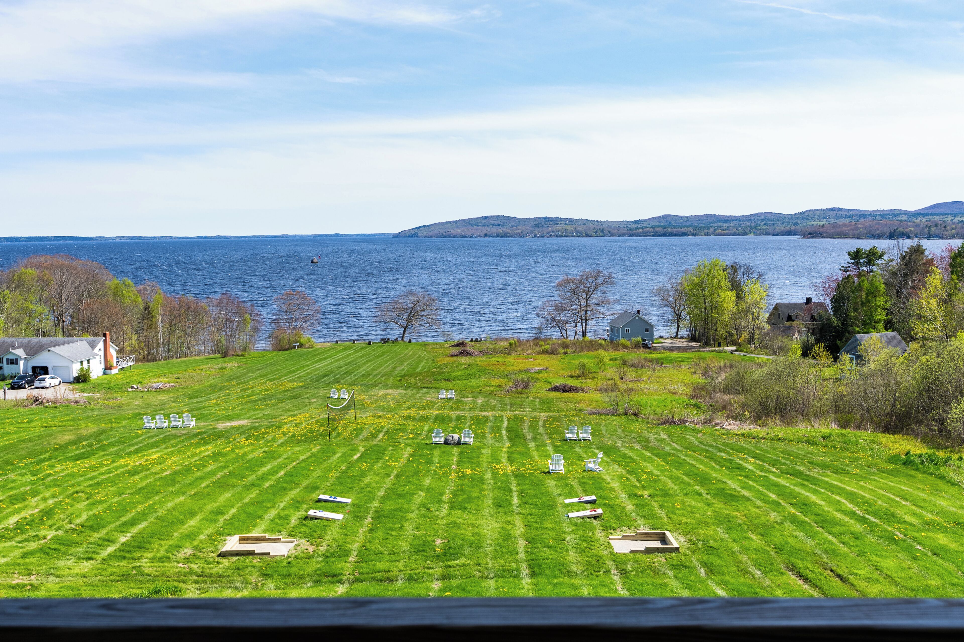 A grassy field with several chairs arranged in rows, overlooking a body of water and distant hills.