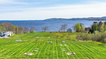 A grassy field with several chairs arranged in rows, overlooking a body of water and distant hills.
