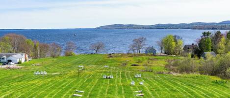 A grassy field with several chairs arranged in rows, overlooking a body of water and distant hills.