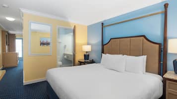 A hotel room with a large bed, a nightstand with a lamp, a wooden headboard, and a bathroom visible through an open door.