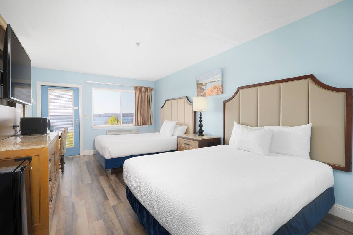 A hotel room with two beds, a desk with a microwave, a TV, and a window with curtains.