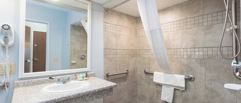 A bathroom with a granite countertop sink, a mirror, a shower with a glass door, and a tiled floor.