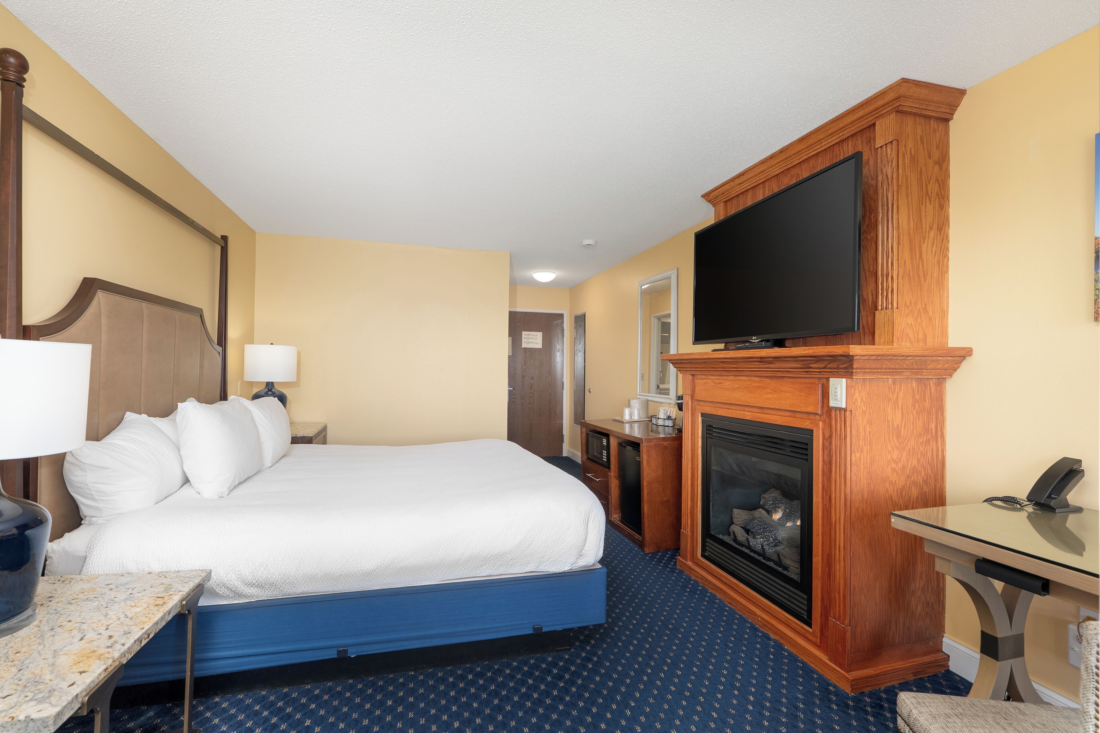 A hotel room with a bed, a television, a fireplace, a desk, and a chair.