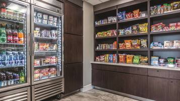 A snack and beverage refrigerator stocked with various drinks and snacks, and a shelf with packaged food items.