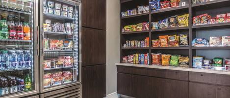 A snack and beverage refrigerator stocked with various drinks and snacks, and a shelf with packaged food items.