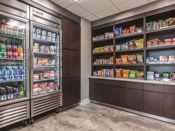 Un refrigerador con bebidas y aperitivos, repleto de diversas opciones, además de una estantería con alimentos envasados.
