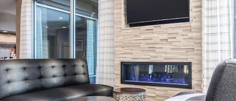 Un moderno salón con un sofá de cuero negro, dos mesitas de noche estampadas, un televisor de pantalla plana montado en una pared con diseño de ladrillo y una chimenea.