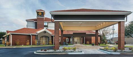 A hotel with a covered entrance, a prominent sign, and a landscaped driveway.