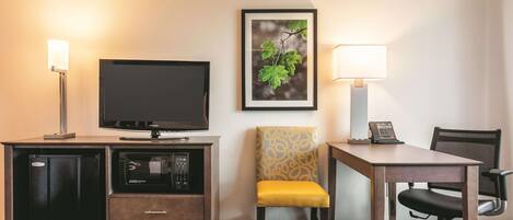 Habitación de hotel con televisión de pantalla plana, escritorio con lámpara, una silla y una mesita.