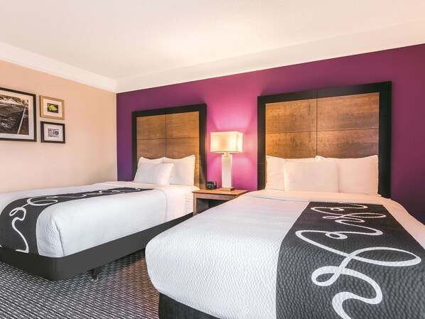 Quarto de hotel com duas camas, uma mesa de cabeceira com abajur e uma parede com quadros.