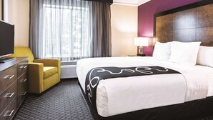 Quarto de hotel com cama, televisão, escrivaninha, cadeira e janela com cortinas.