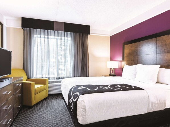 A hotel room with a bed, a TV, a desk, a chair, and a window with curtains.