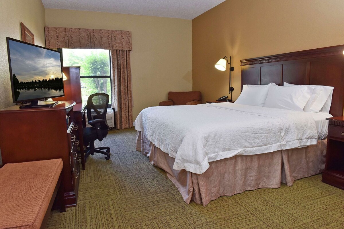 A hotel room with a bed, desk, chair, TV, and a window with curtains.