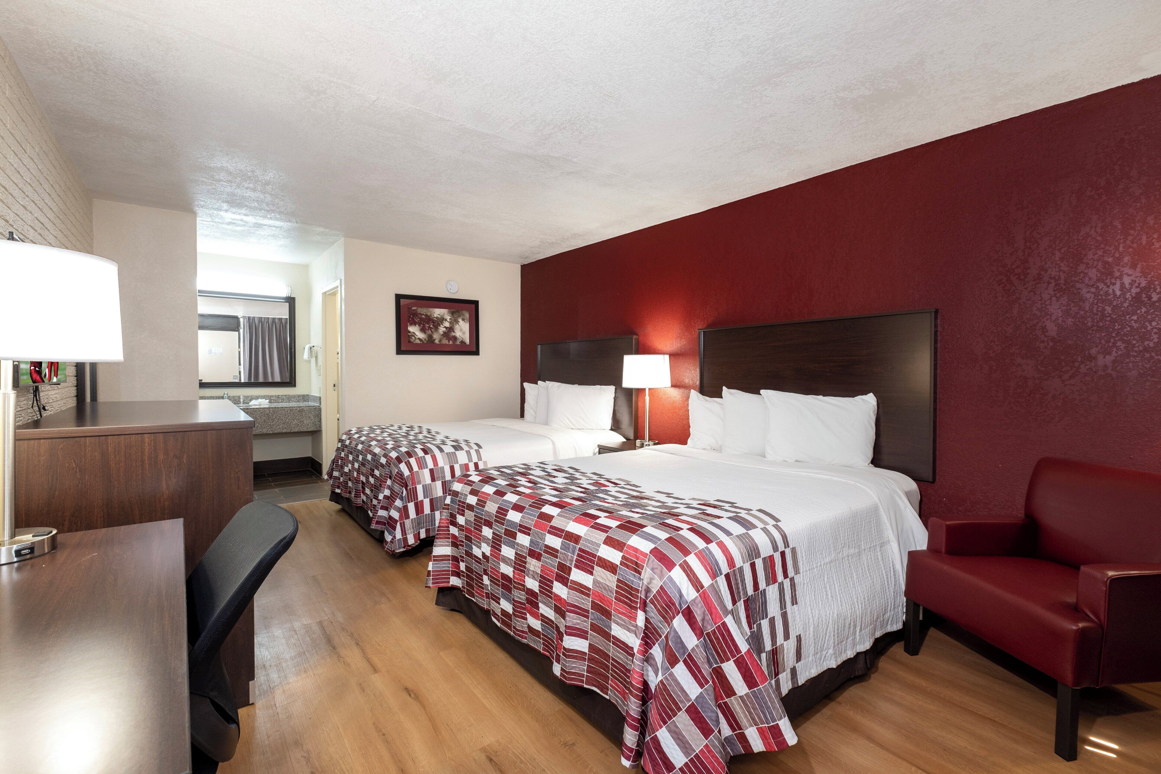 Une chambre d’hôtel avec deux lits, un bureau, une chaise et un mur rouge.