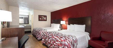 A hotel room with two beds, a desk, a chair, and a red wall.