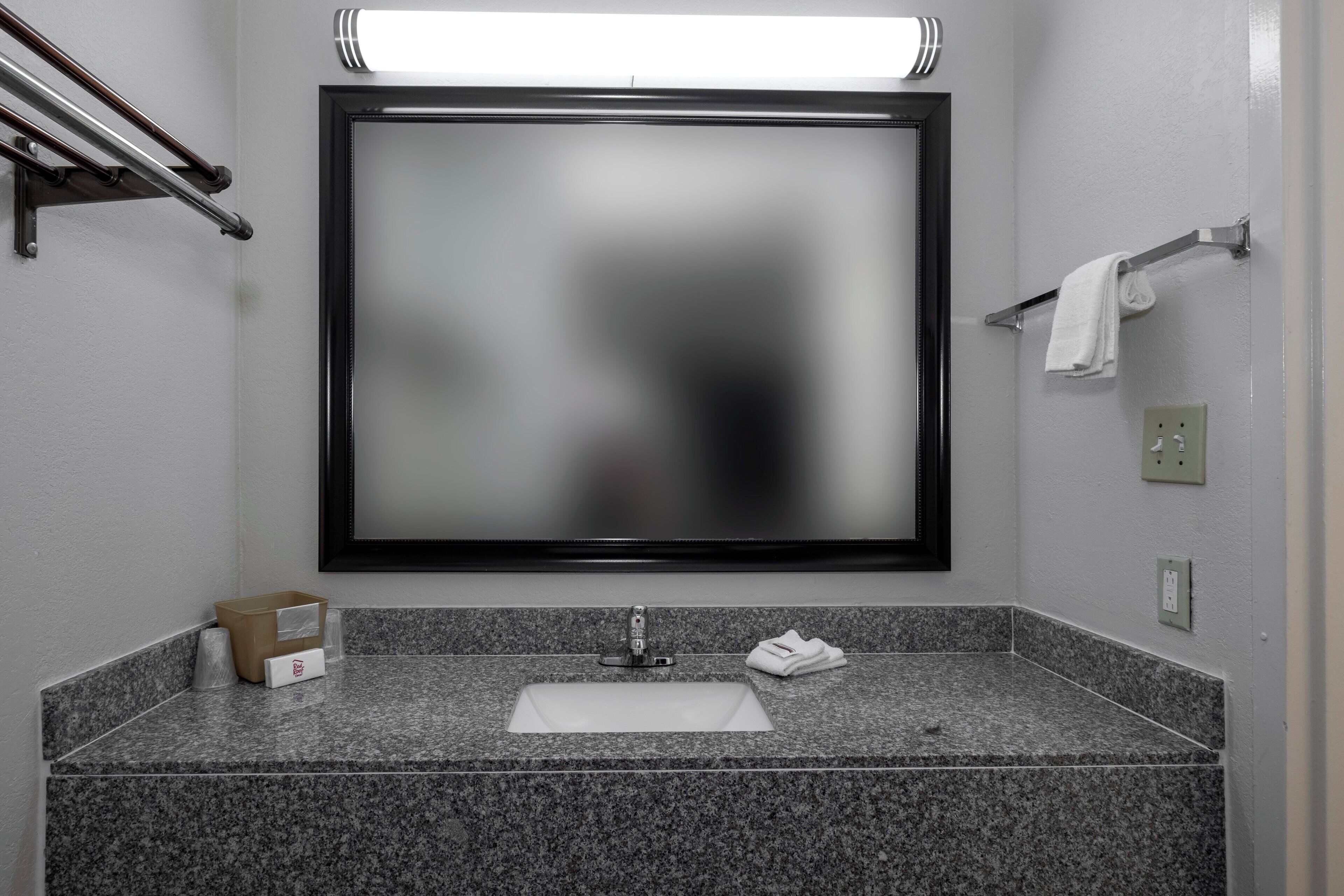 Uma casa de banho com um espelho grande, uma pia, um porta-toalhas e um cesto de lixo.