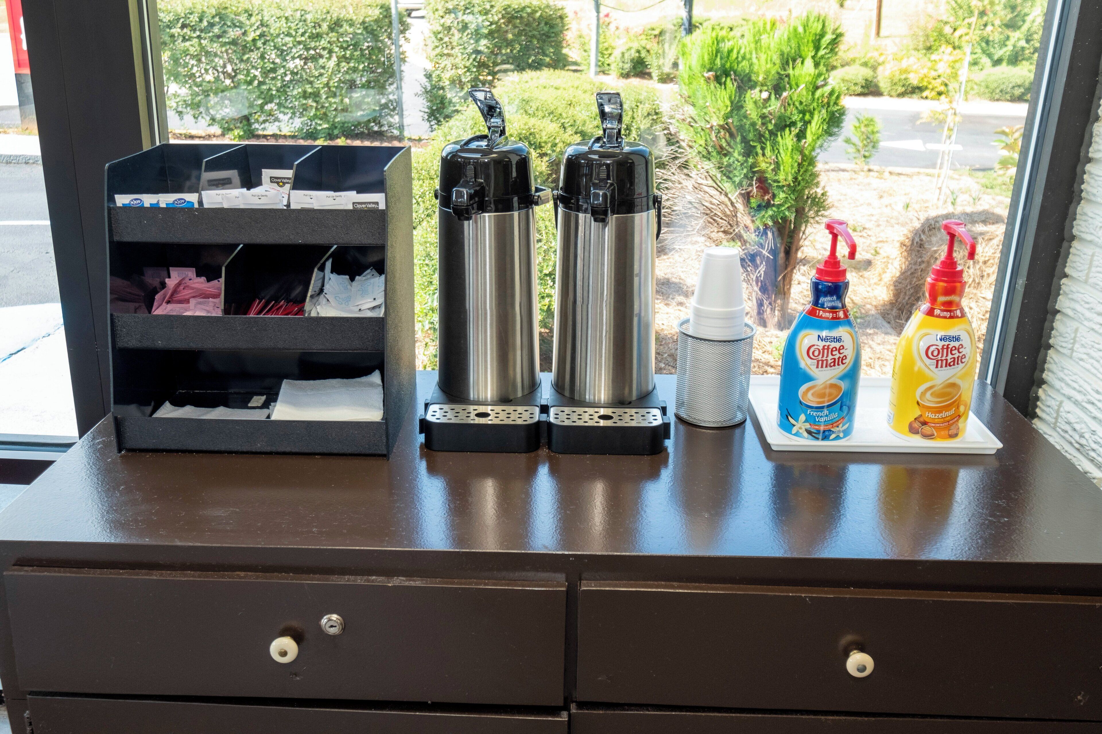 Una estación de café con dos hervidores eléctricos, un molinillo de café y dos recipientes de Nestle Coffee-Mate.