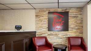 A Red Roof Inn reception area with a brick wall, a reception desk, and two red leather chairs. - Red Roof Inn West Point (West Point)