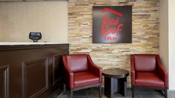 Zona de recepción de Red Roof Inn con pared de ladrillo, un mostrador de recepción y dos sillones de cuero rojo.