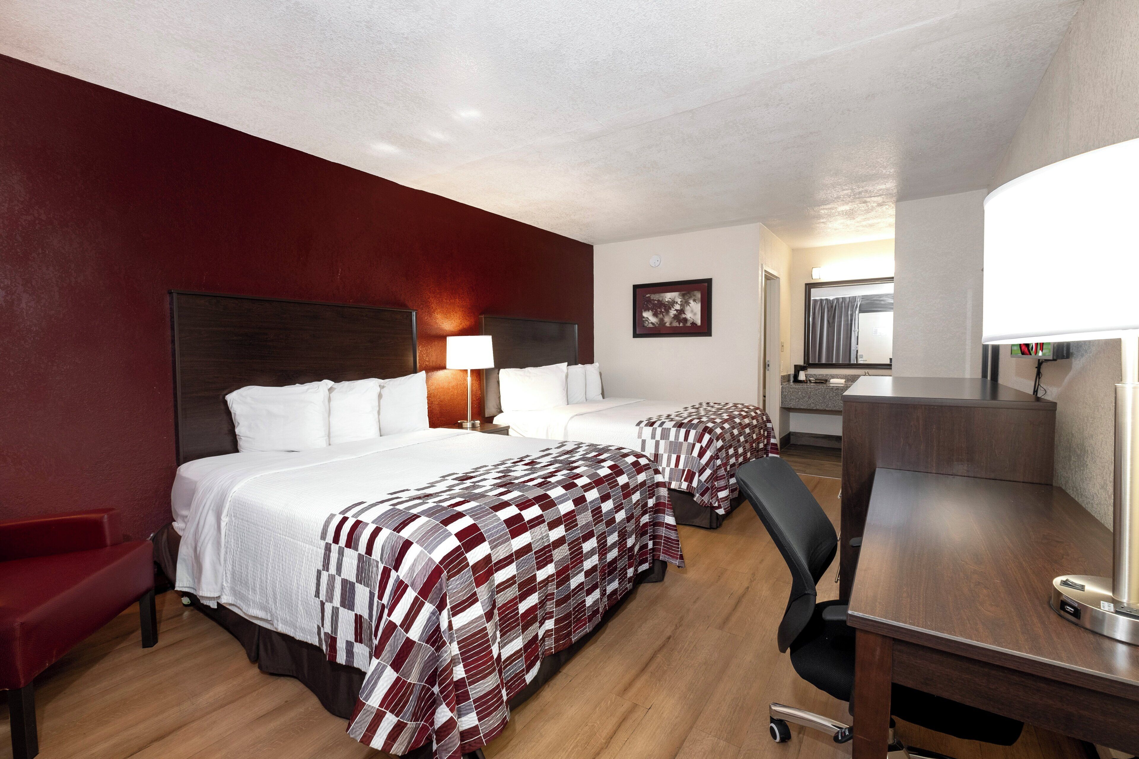 Een hotelkamer met twee bedden, een bureau, een stoel, een lamp en een schilderij aan de muur.
