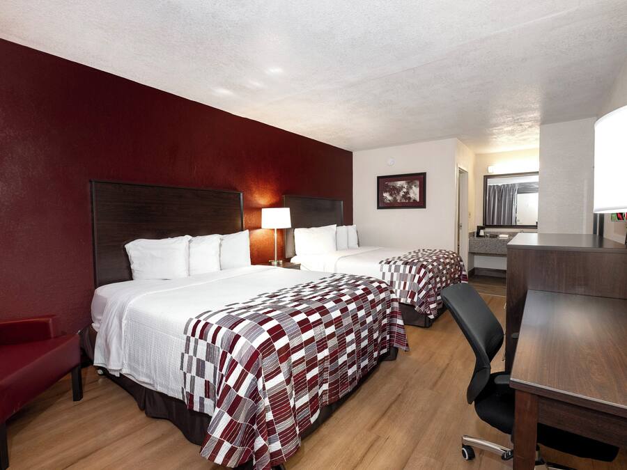 Habitación de hotel con dos camas, un escritorio, una silla, una lámpara y un cuadro en la pared.