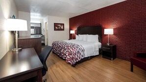 A hotel room with a bed, bedside lamps, a desk, a chair, and a red brick wall. - Red Roof Inn West Point (West Point)