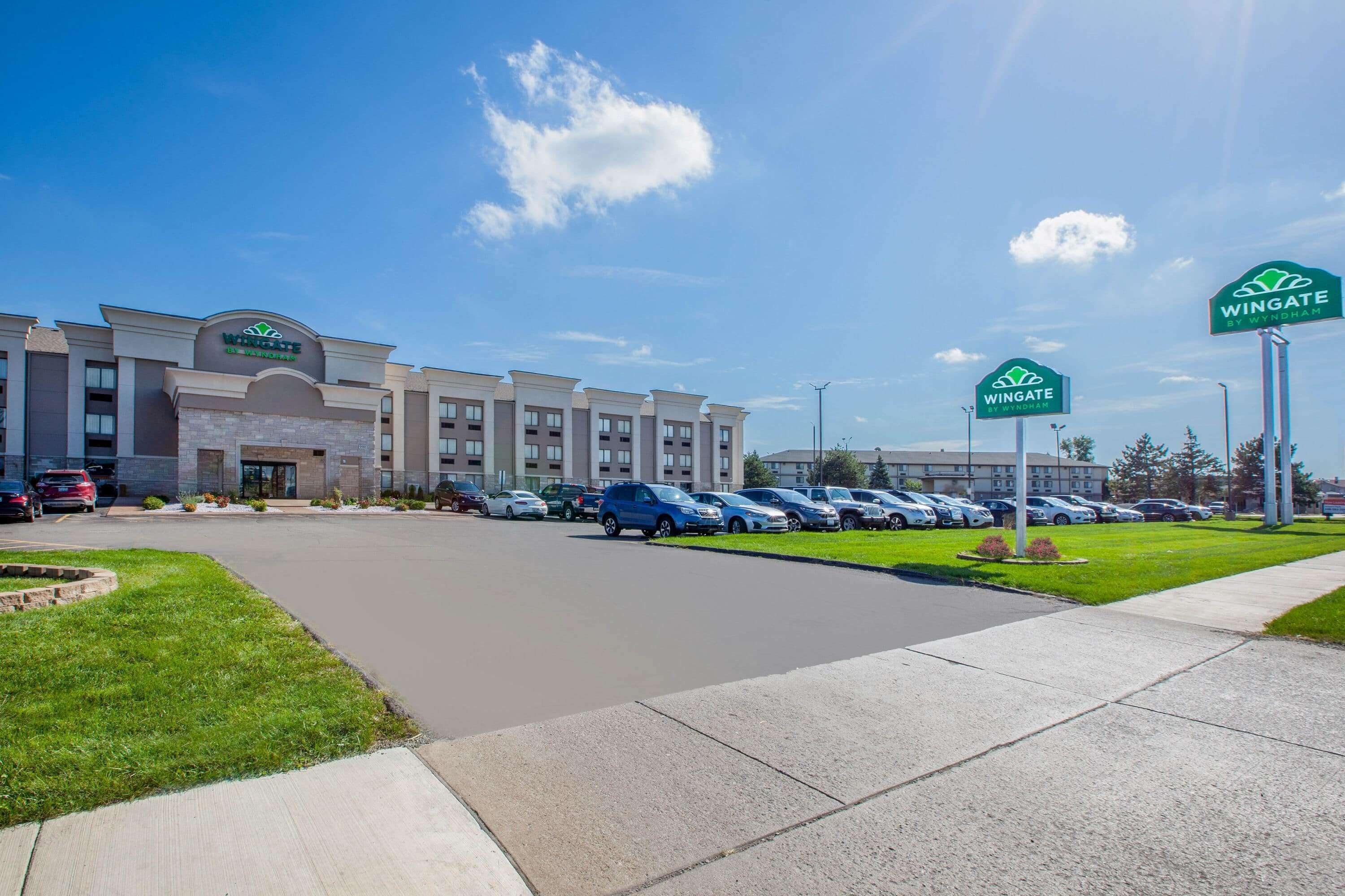 Un hotel Wingate by Wyndham con estacionamiento, varios automóviles y un cielo azul despejado.
