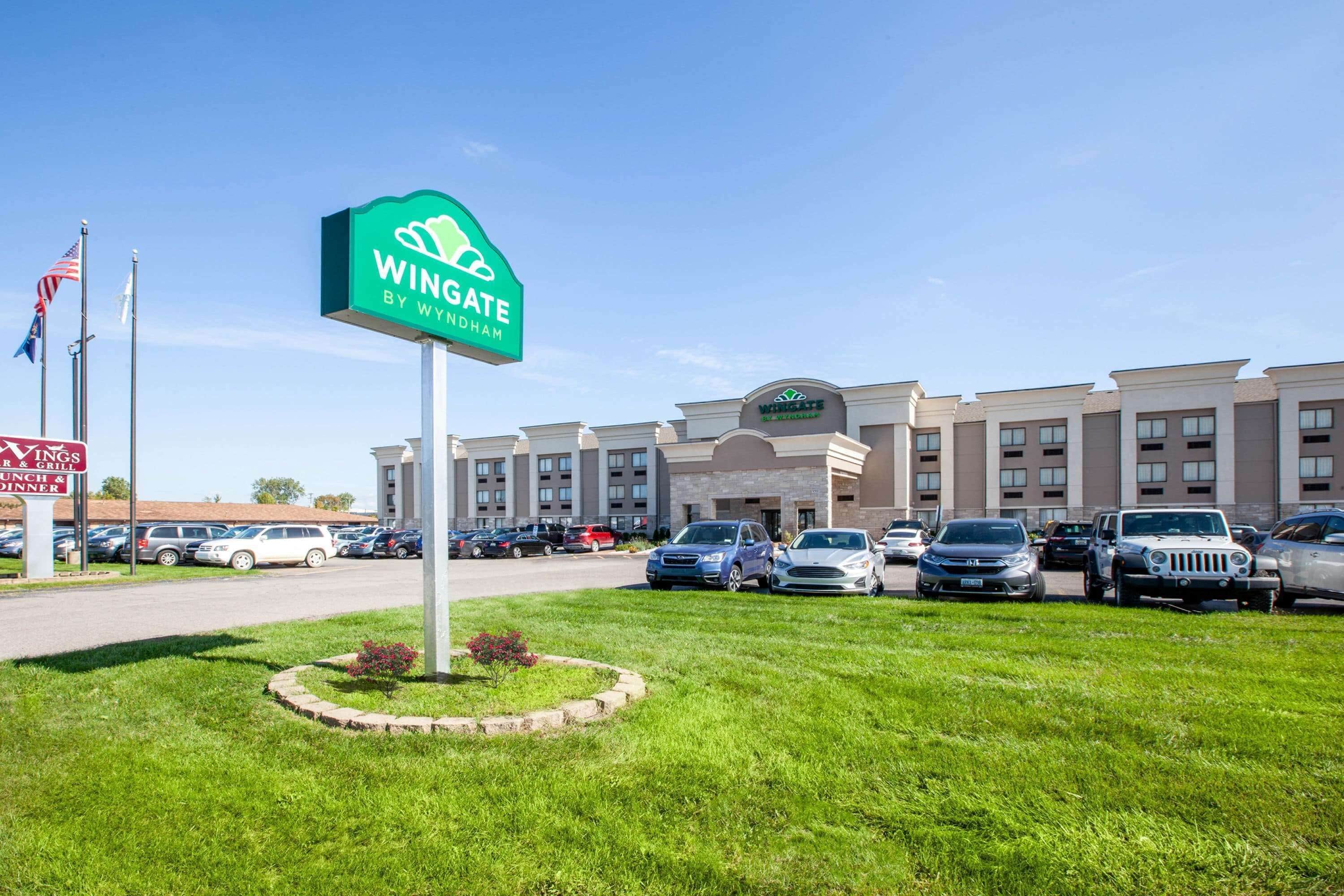 Un hotel con un letrero verde que dice 'Wingate by Wyndham' y un estacionamiento con varios coches.