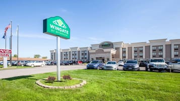 Un hotel con un letrero verde que dice 'Wingate by Wyndham' y un estacionamiento con varios coches.