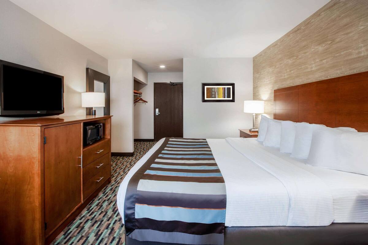 A hotel room with a large bed, a television, a wardrobe, and a desk with a lamp.