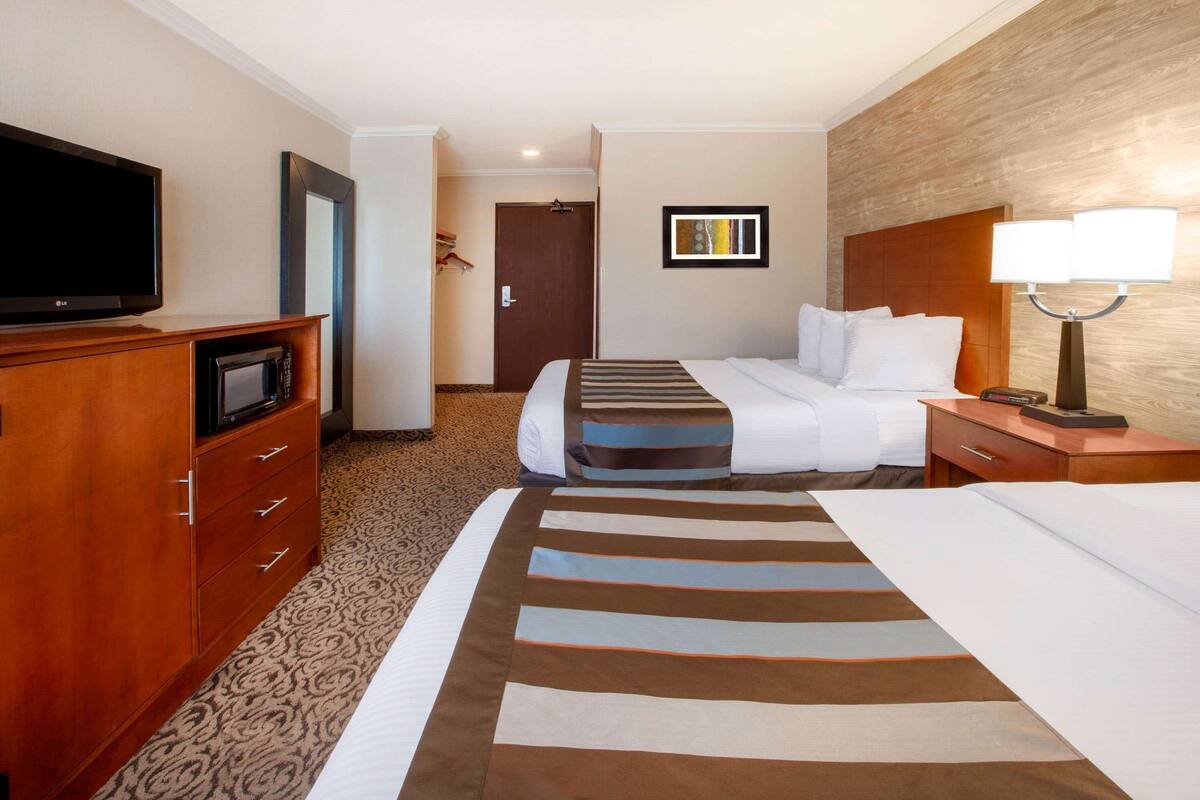 A hotel room with a bed, a TV, a desk with a lamp, and a wardrobe.
