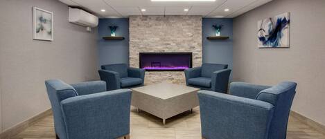 A room with a stone fireplace, blue upholstered chairs, a central coffee table, and recessed lighting.