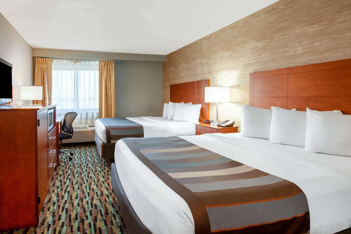 A hotel room with two beds, a desk, a chair, a TV, and a window with curtains.