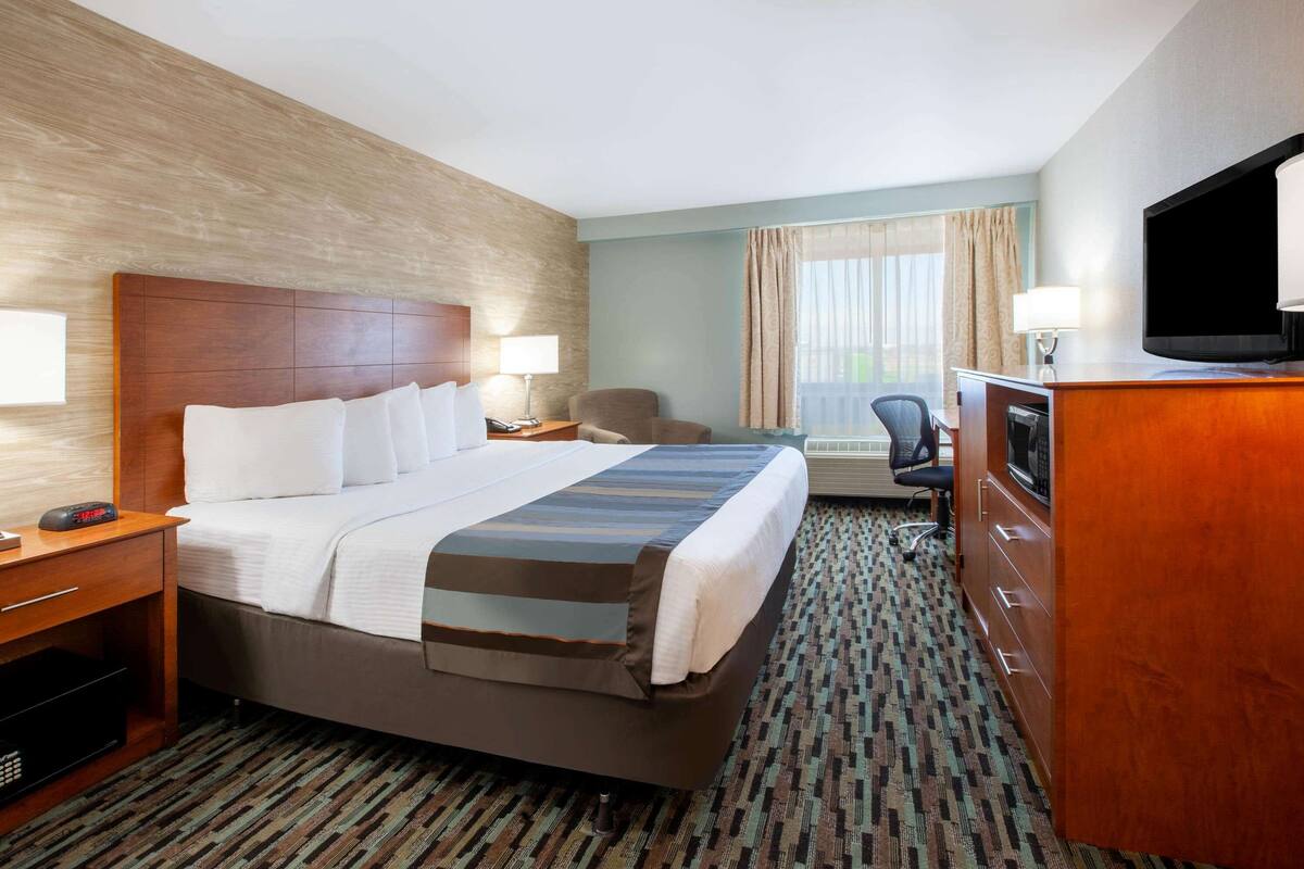 A hotel room with a large bed, a desk with a television, a chair, and a window with curtains.