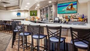 A bar area with a long counter, multiple stools, and a variety of bottles.